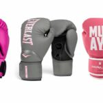 Três luvas de boxe feminina de marcas diferentes em cores rosa, cinza e preta, dispostas sobre fundo branco.
