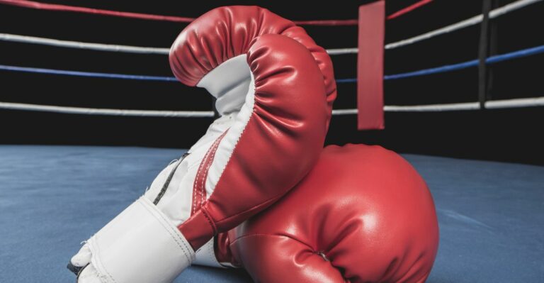 Par de luvas de boxe vermelhas sobre as cordas de um ringue profissional, equipamento essencial para treinos e competições de boxe e Muay Thai