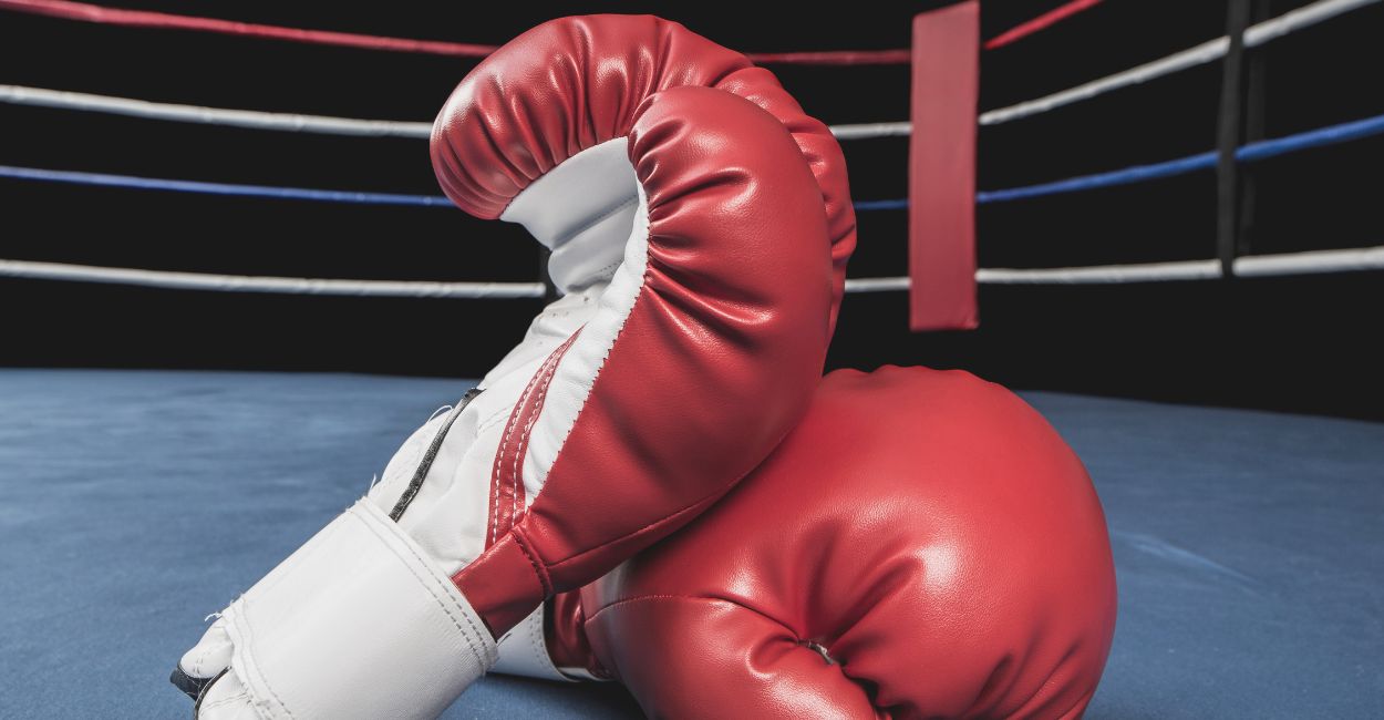 Par de luvas de boxe vermelhas sobre as cordas de um ringue profissional, equipamento essencial para treinos e competições de boxe e Muay Thai