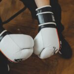 Pessoa usando luvas de boxe pretas, com os braços posicionados em guarda de combate, pronta para treino ou luta.