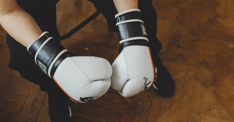 Pessoa usando luvas de boxe pretas, com os braços posicionados em guarda de combate, pronta para treino ou luta.